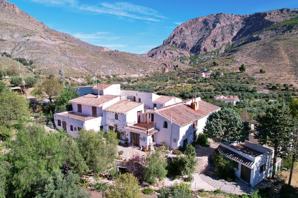 Scenic view of a large white country house with red-tiled roof, surrounded by mountains under a clear Spanish sky