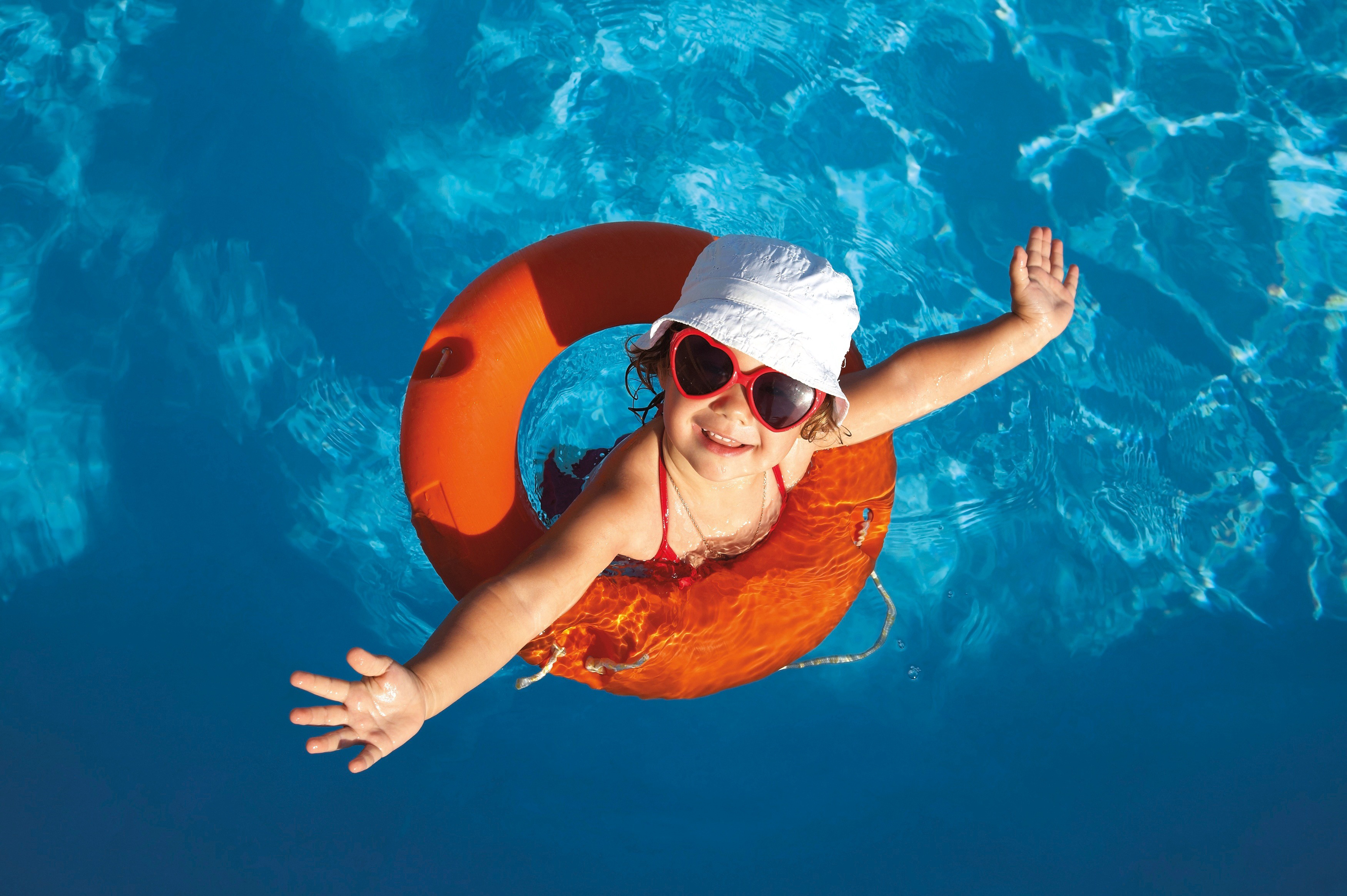 Young girl floating in a swimming pool with an orange lifebuoy, wearing a red swimsuit