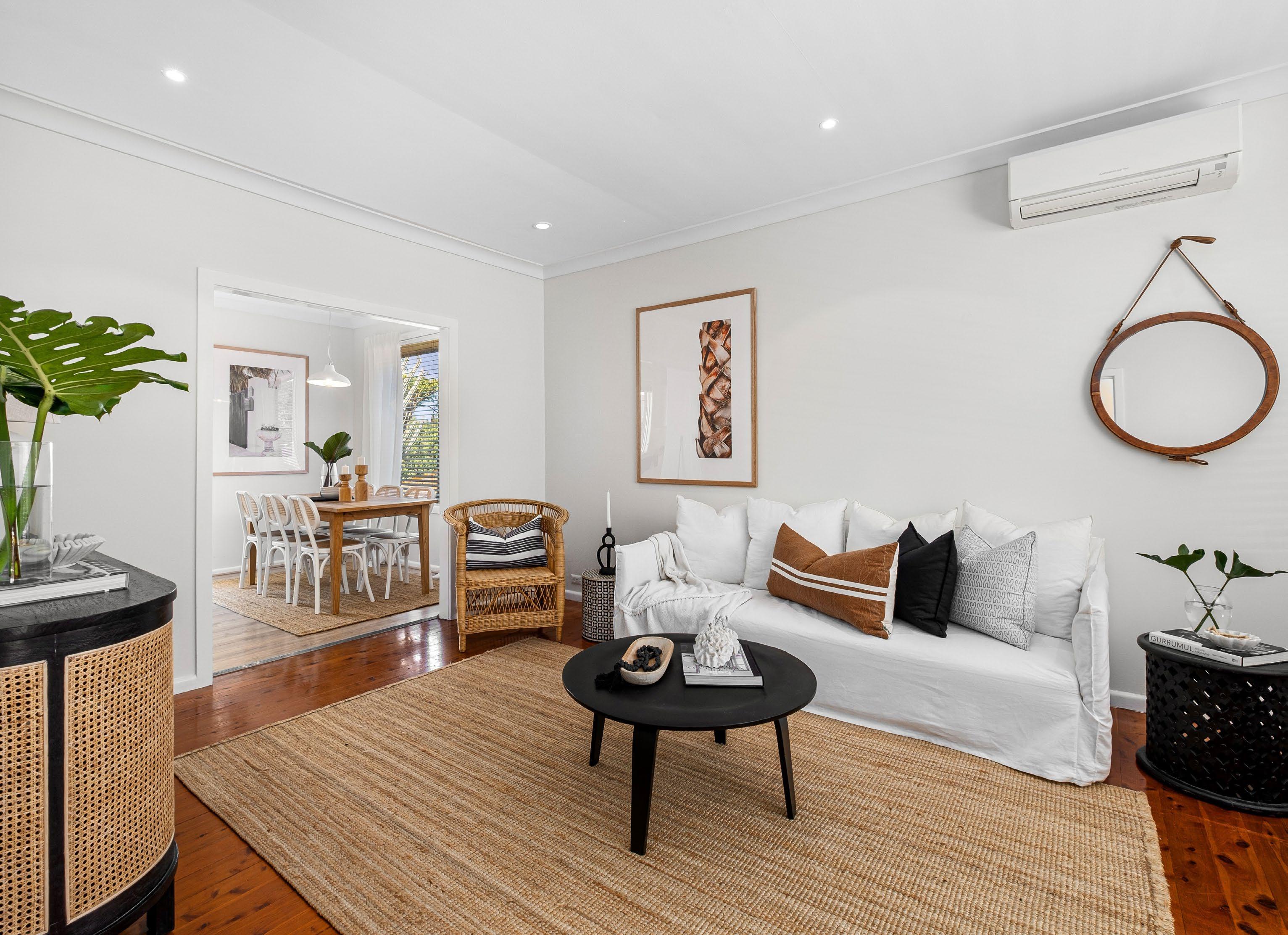 A clean and organized living room with a couch, coffee table, and wicker chair. This inviting space is ready to be staged for a home sale.