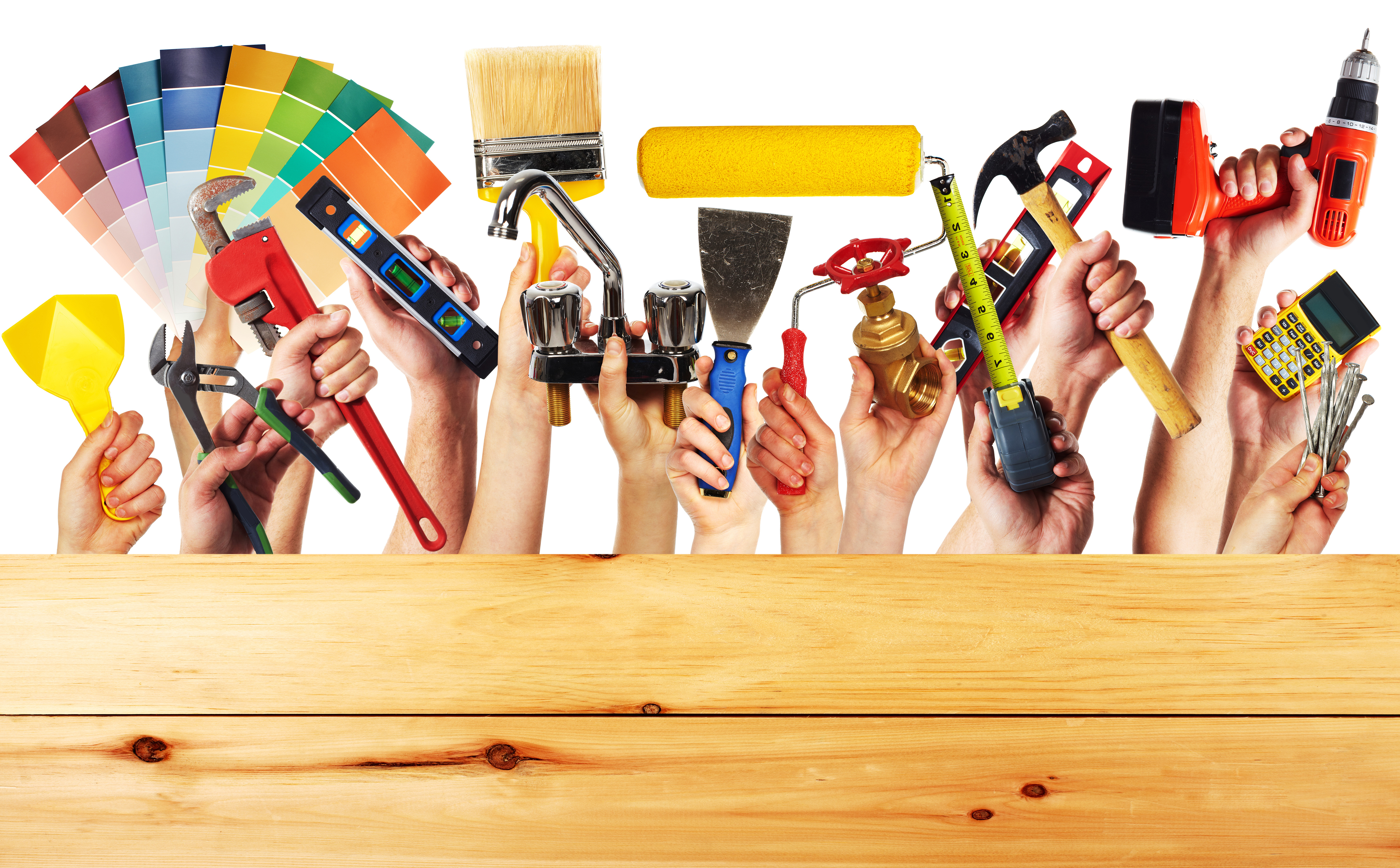 Group of diverse hands holding various construction tools over a wooden work table. The tools include a hammer, saw, screwdriver, wrench, and paintbrush.